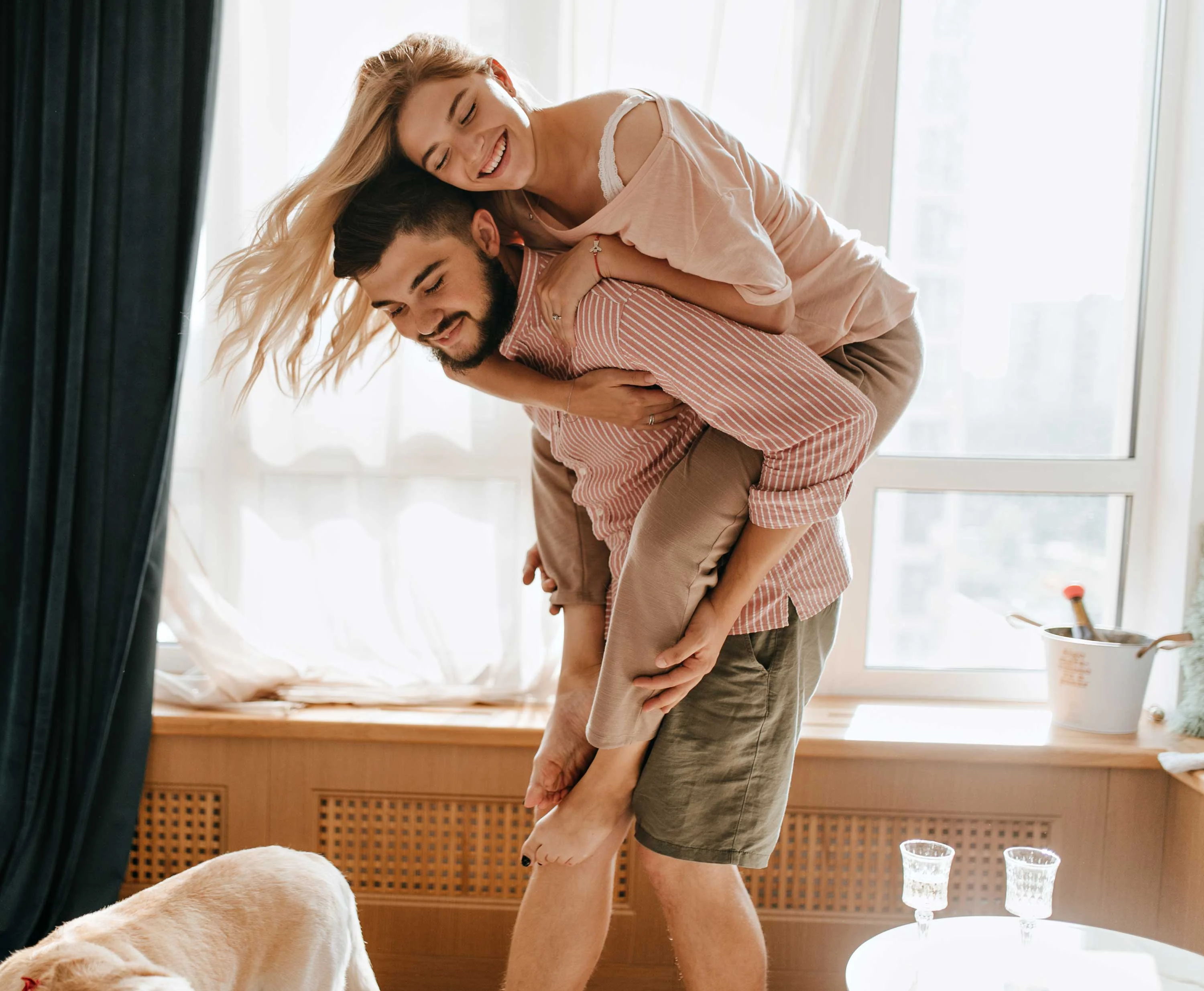 A man giving a piggyback ride to a smiling woman in a bright indoor setting.