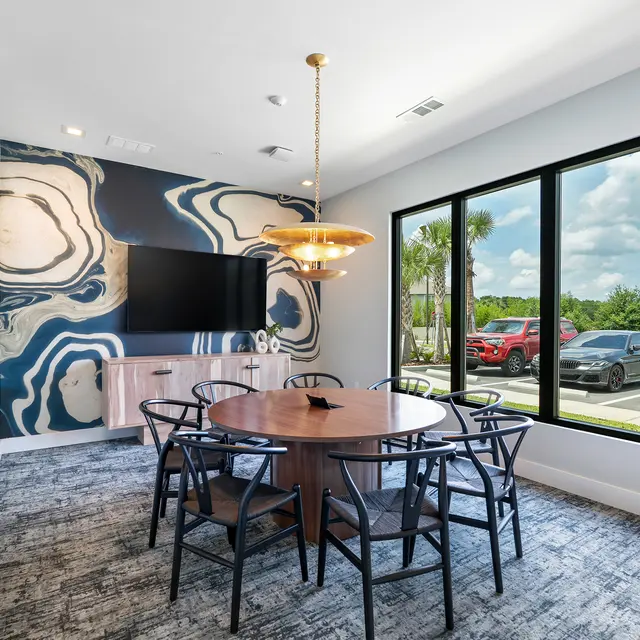 Modern Meeting Room Interior A stylish meeting room featuring a round wooden table surrounded by black chairs. A large window offers a view of the outdoors, with modern decor on the walls and a TV mounted on one side.