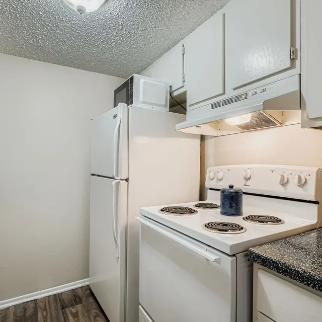 A compact kitchen featuring a white refrigerator, stove, and microwave, with granite countertops and wooden flooring.