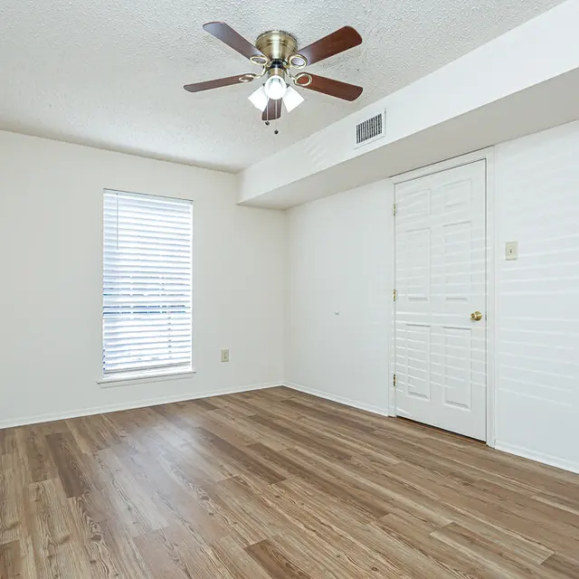 An empty room featuring a ceiling fan, a window with blinds, and wooden flooring.