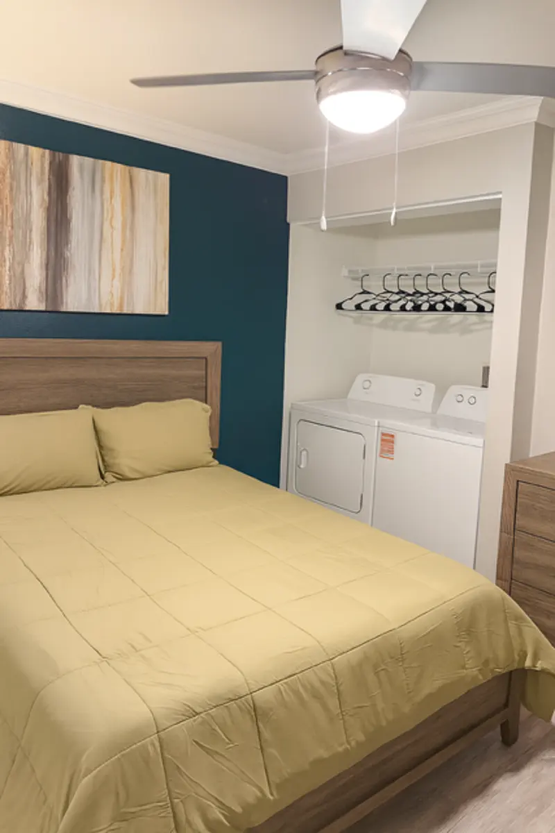 Cozy Bedroom with Laundry Facilities A cozy bedroom featuring a yellow bedspread, a wall with teal paint, and a small laundry area with a washer and dryer