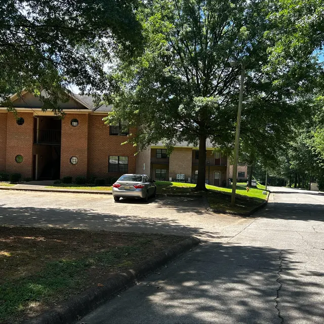Residential Area with Brick Apartments View of a residential area with brick apartment buildings, trees, and a parked car on a sunlit street.