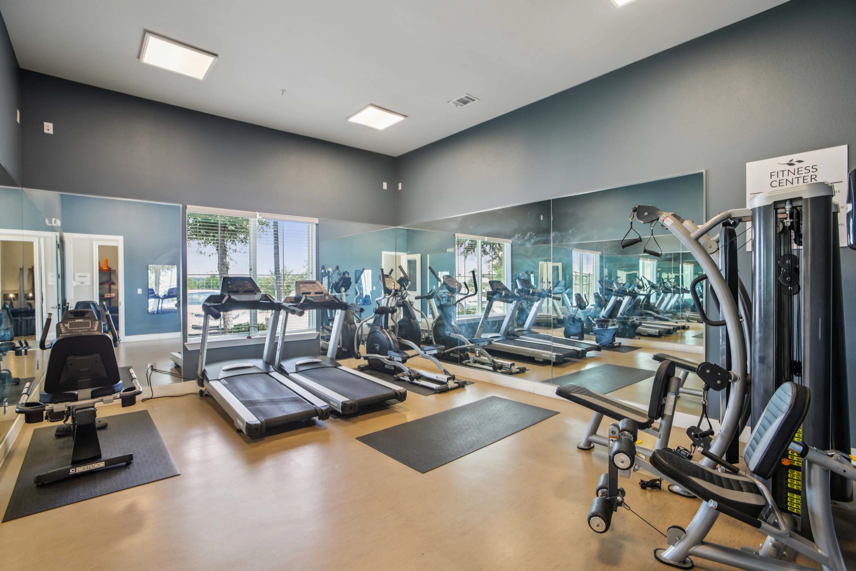Modern Fitness Center A modern fitness center with various gym equipment including treadmills, a multi-gym machine, and exercise mats. Large windows allow natural light to fill the space, and mirrors line the walls.