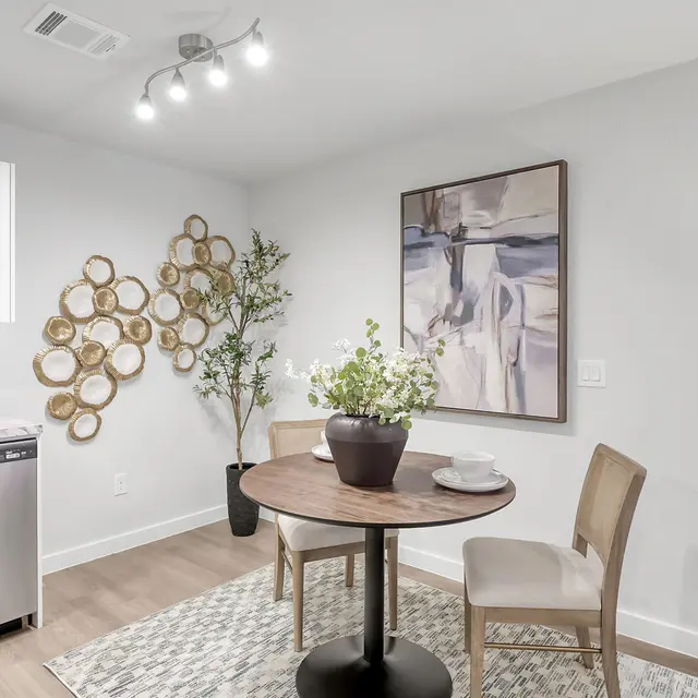 A stylish small dining area with a round table, two chairs, and a decorative wall featuring circular art pieces and a painting.