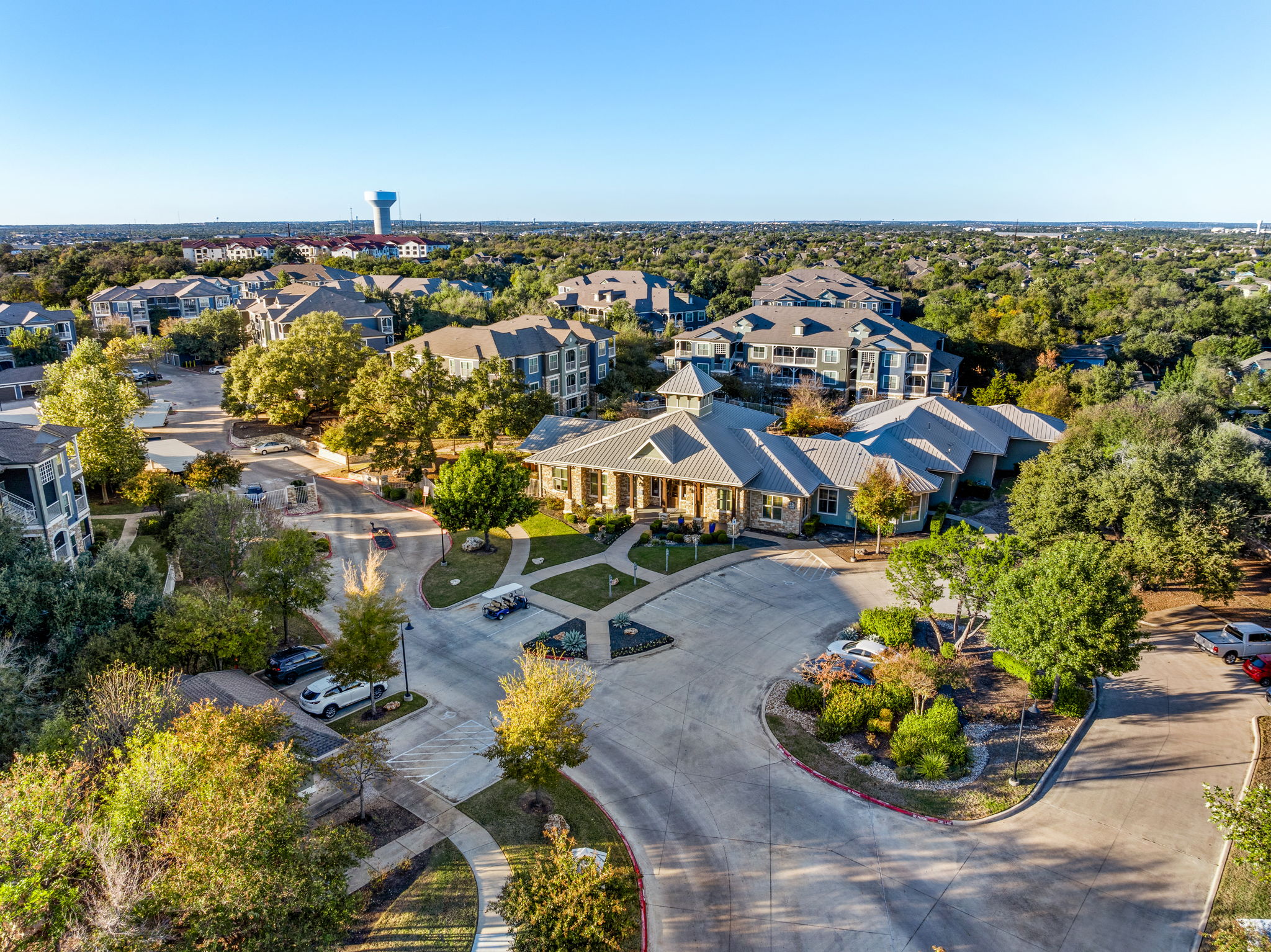 Aerial view of a residential community with multiple buildings and green spaces, including parking areas and trees.