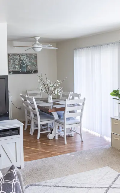 Bright living room with a dining area featuring a large TV, white dining table, and potted plants.