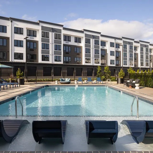A modern apartment complex with a swimming pool and lounge chairs