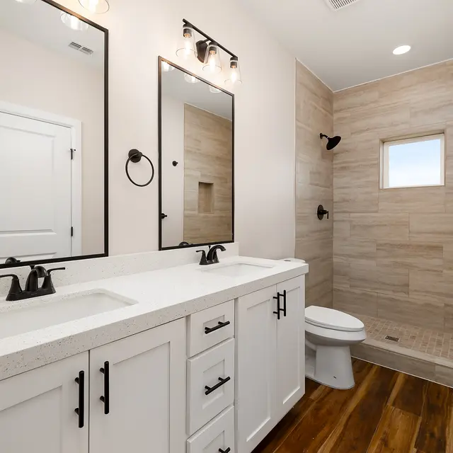A modern bathroom featuring dual sinks, mirrors, a stand-up shower with a small window, and wooden flooring.