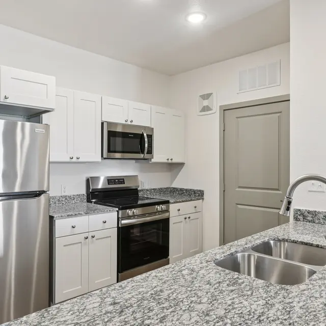 A modern kitchen featuring stainless steel appliances, including a refrigerator and oven, with white cabinets and granite countertops.