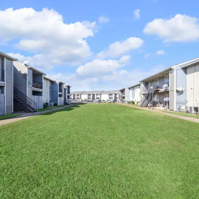 View of an apartment complex with two-story buildings and a grassy area in the foreground.