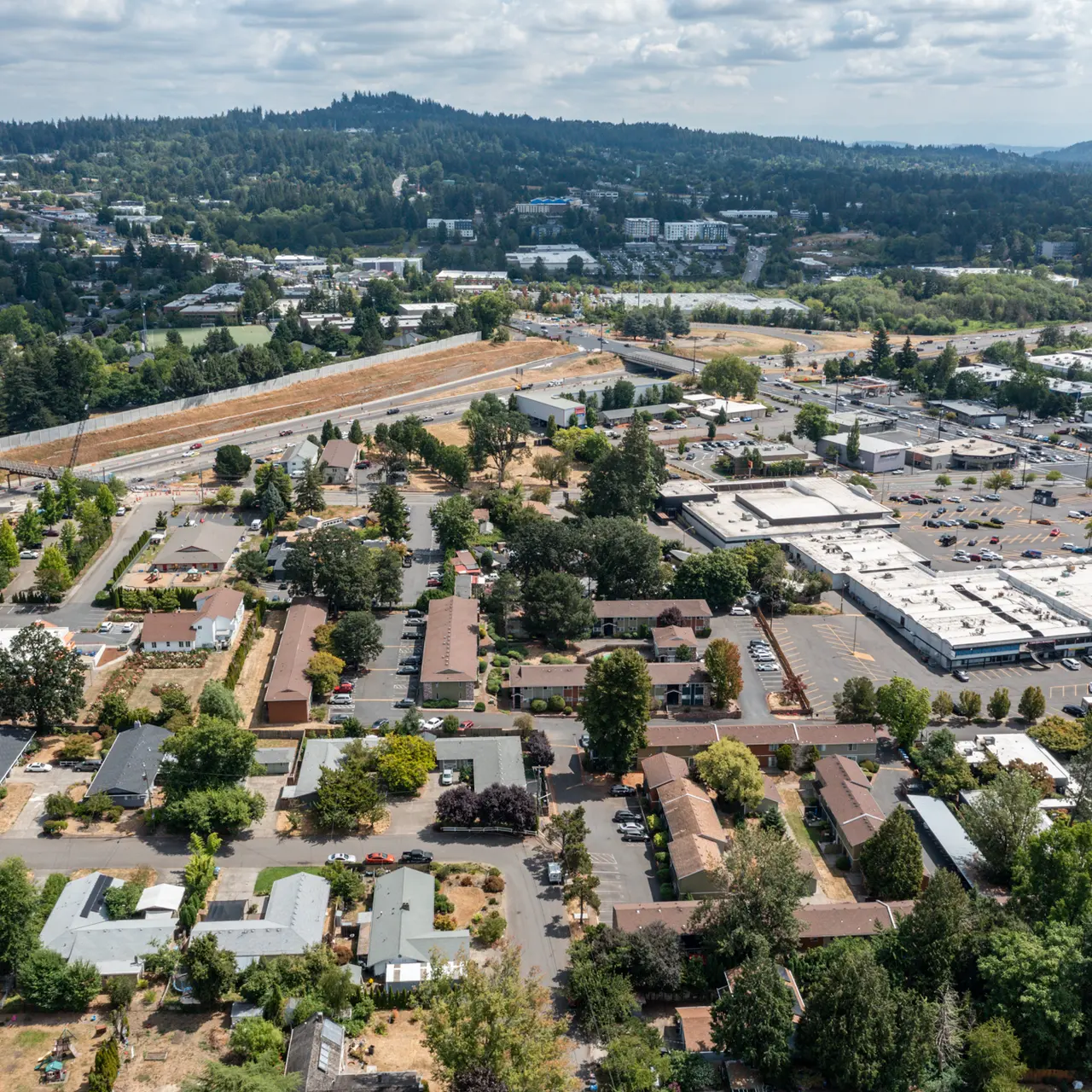 Aerial View of Suburban Neighborhood and Commercial District Aerial view of a suburban area with residential homes, commercial buildings, and green spaces. The landscape shows a mix of developed and natural land.