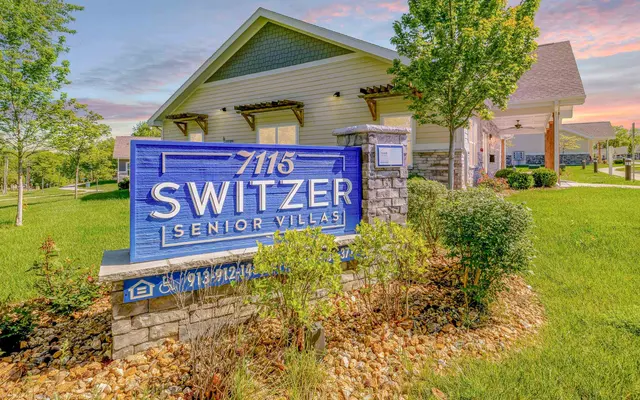 Switzer Senior Villas Sign A blue sign for Switzer Senior Villas, surrounded by green grass and trees, with a building in the background.