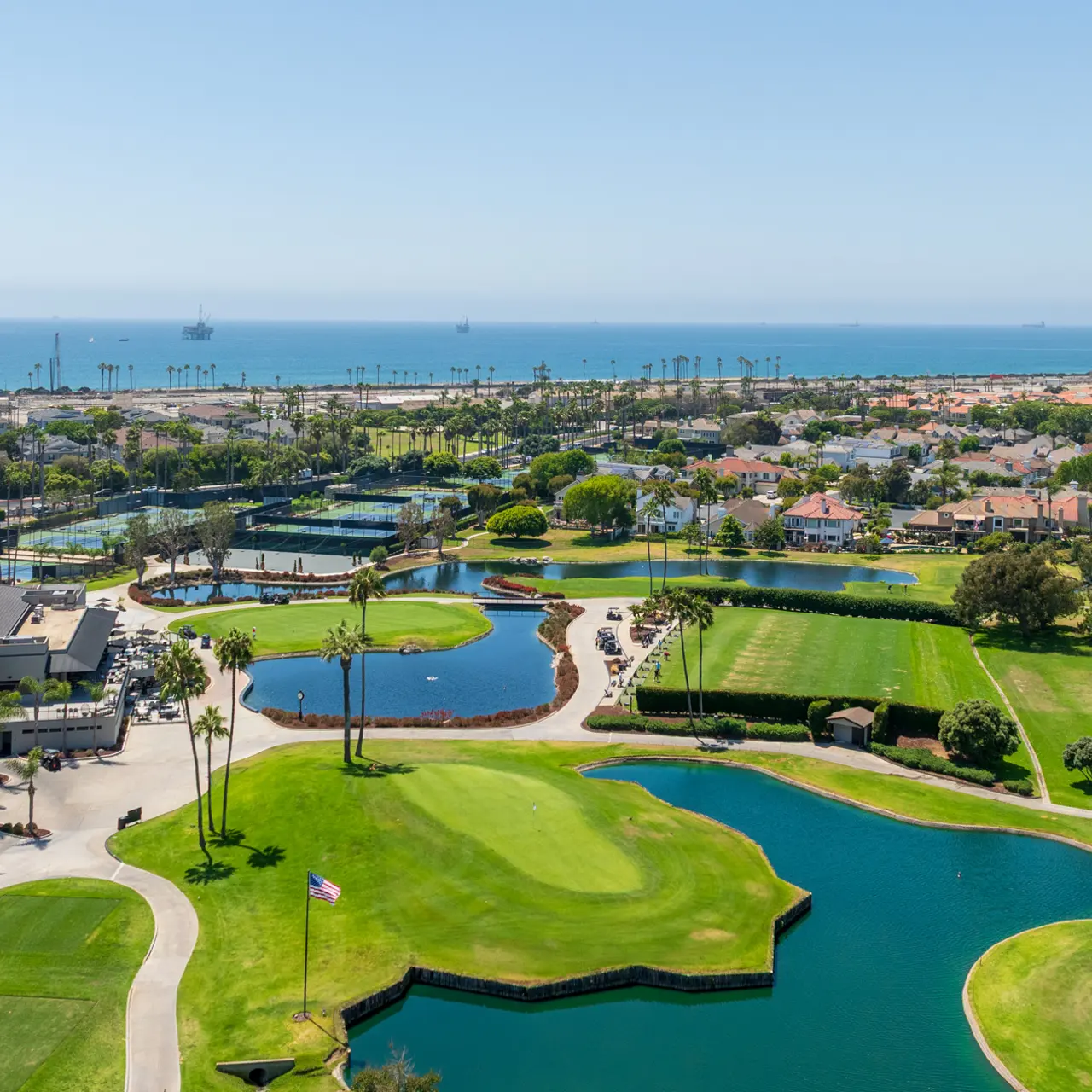Aerial view of a coastal golf course with large green areas and water features, overlooking the ocean.