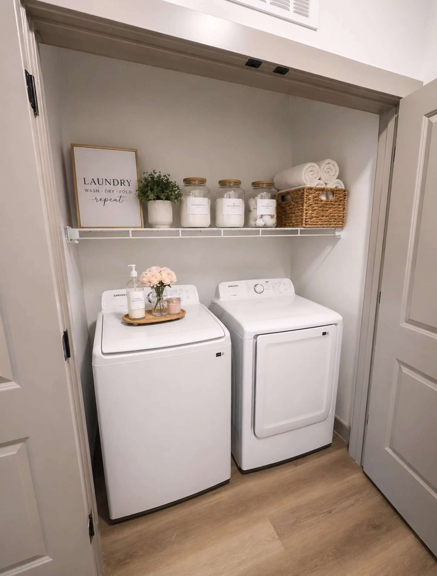 Stylish Laundry Room Organization A neatly organized laundry room with a washer and dryer side by side, shelves above holding decorative containers and towels, and a framed sign that says 'LAUNDRY'.