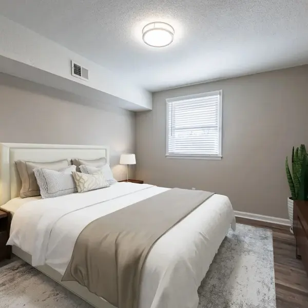 A modern bedroom featuring a queen-sized bed with light-colored bedding, two nightstands with lamps, a window with blinds, and a decorative plant.