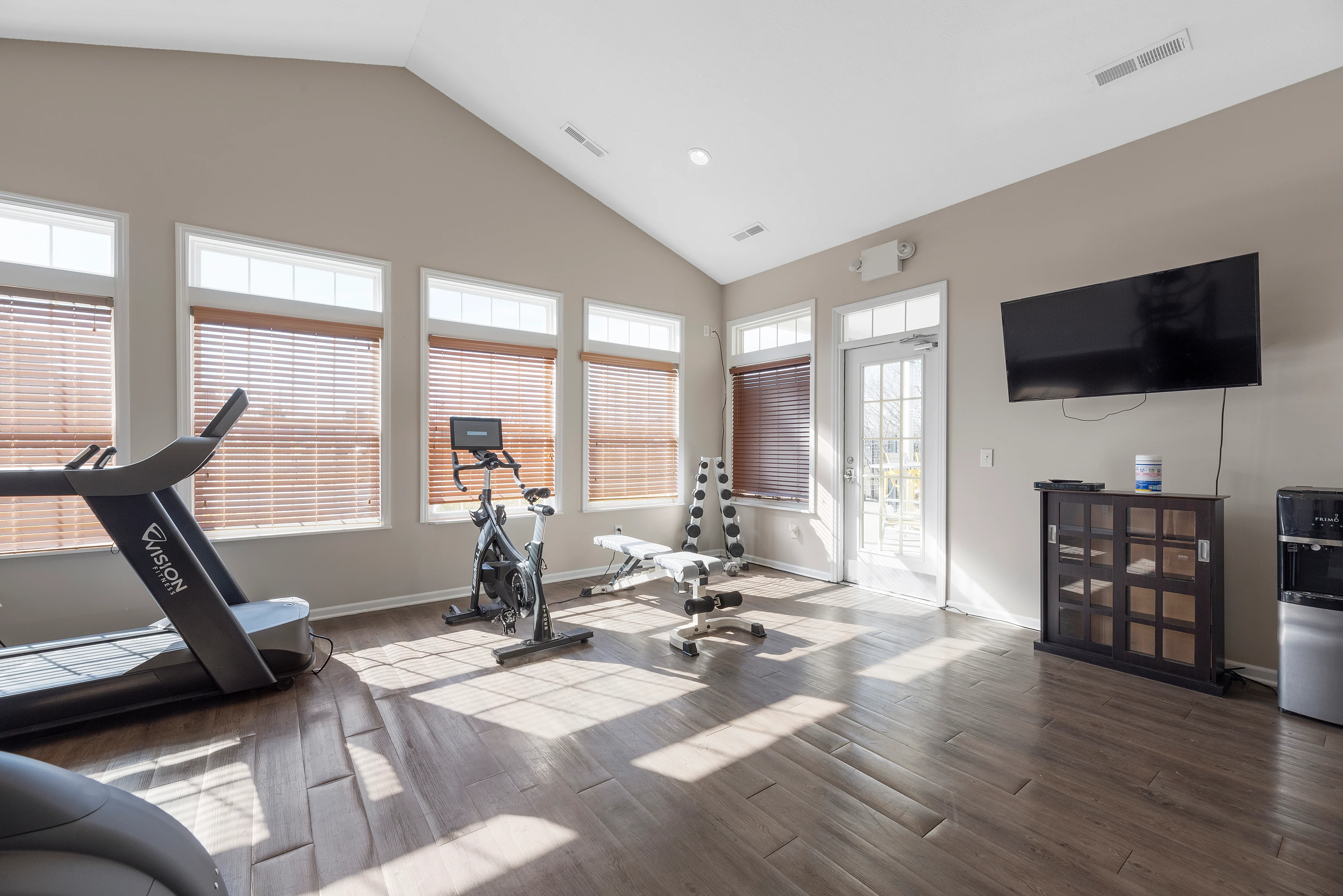A spacious home gym with workout equipment and large windows letting in natural light.