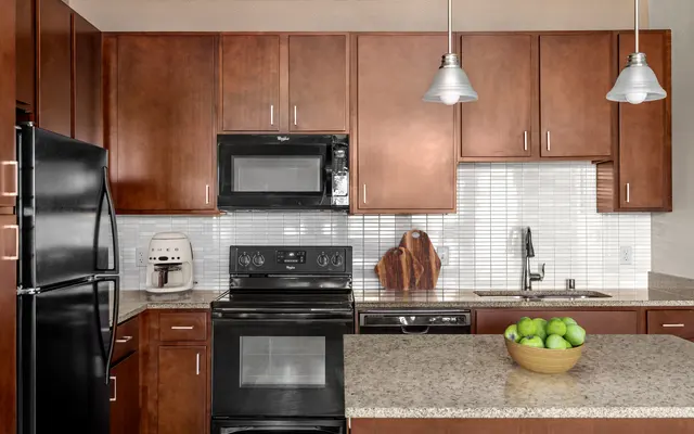 fully equipped kitchen with stainless steel appliances, granite countertops, pendant lamp, and walnut-colored cabinetry at apartments in Kapolei, HI