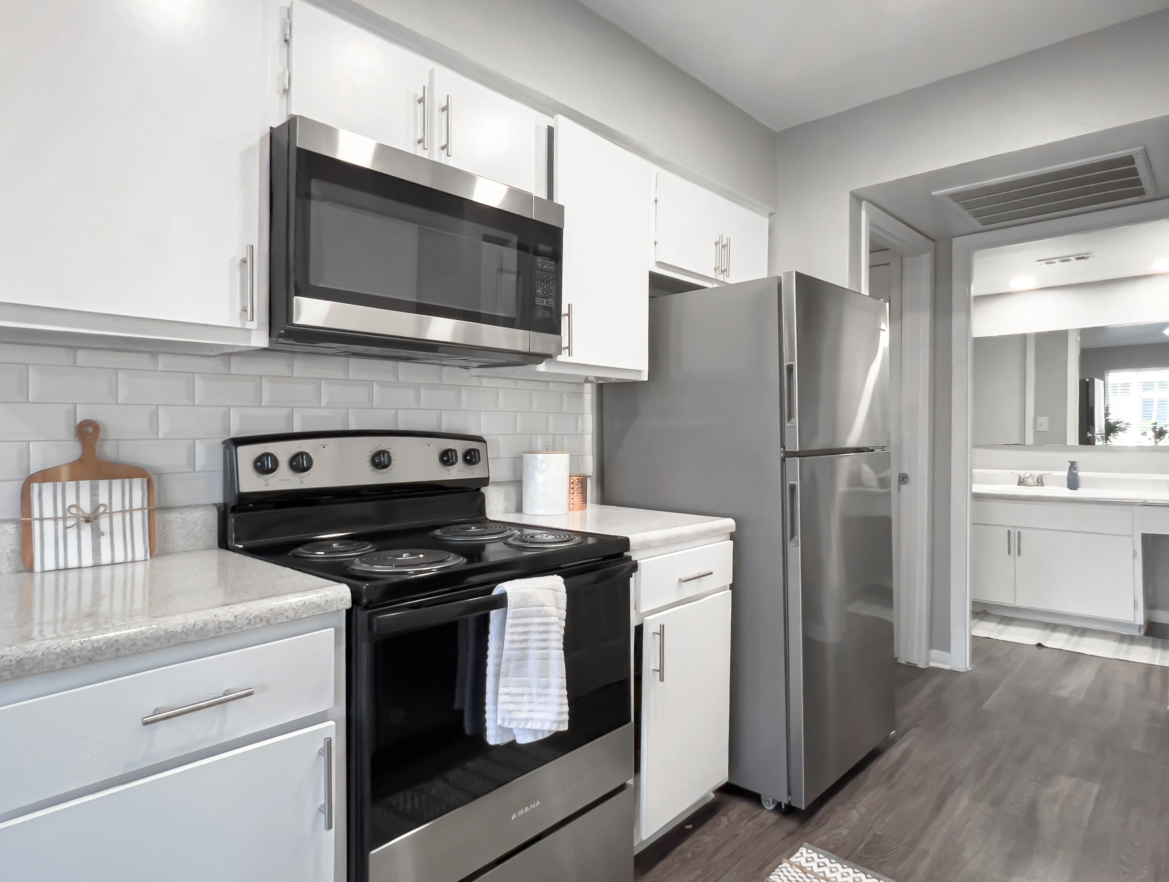 Modern Kitchen Design A modern kitchen featuring sleek white cabinetry and appliances. The kitchen includes a stainless steel microwave above a black stove with a white towel hanging from the oven door, and a silver refrigerator nearby.