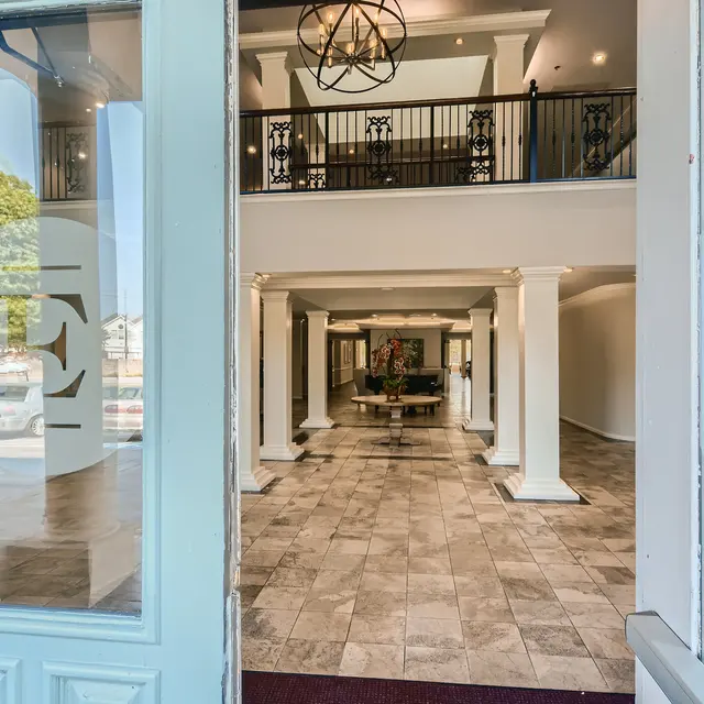View from the entrance of a modern lobby featuring tiled flooring, decorative pillars, and a chandelier above.