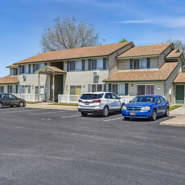 Apartment Building Exterior Exterior view of a two-story apartment building with a tan roof and light colored siding, featuring several parked cars in front.