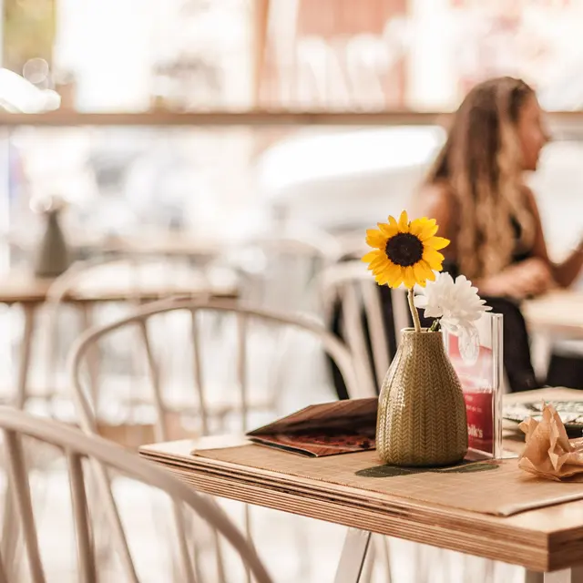 High Street Lofts A cozy café scene with wooden tables, flowers in vases, and blurred patrons enjoying their drinks and conversation.