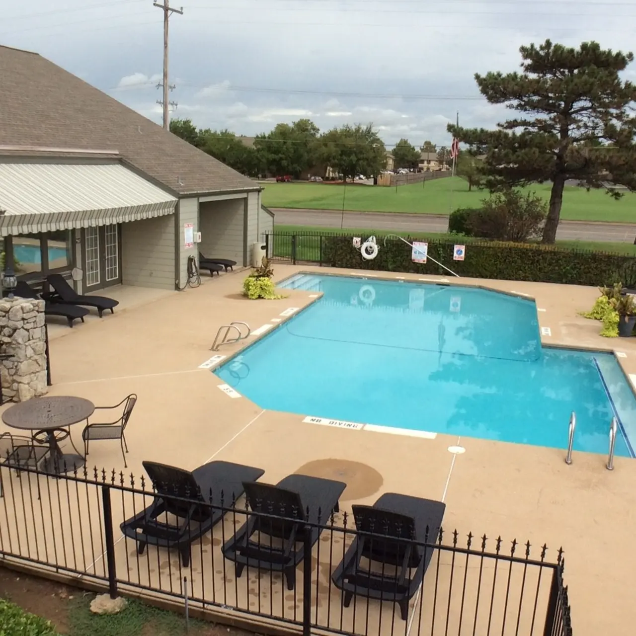 The Hunt Outdoor swimming pool with surrounding patio, lounge chairs, and table. Adjacent building with awning, trees, and grass in the background.