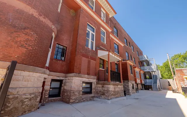 unnamed.webp Exterior view of a brick apartment complex with multiple stories, balconies, and a clear blue sky. - City, Housing, Urban