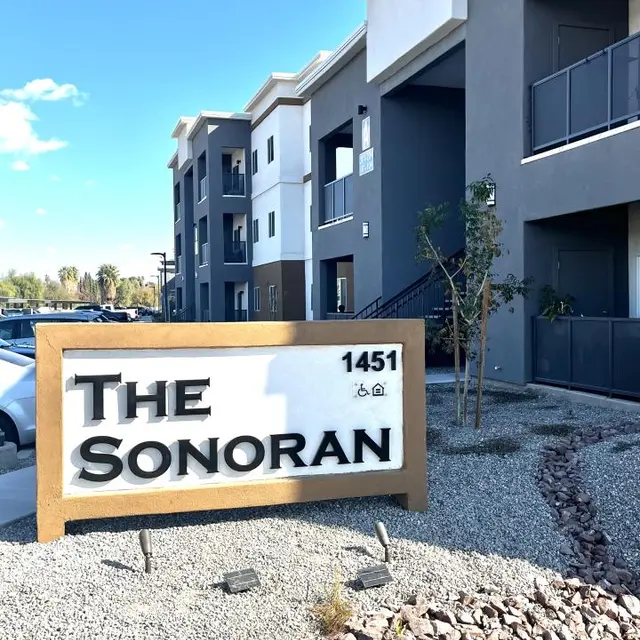 Exterior view of an apartment complex sign that reads 'The Sonoran' with the address '1451', surrounded by gravel and landscaping.