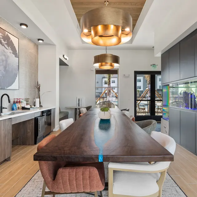 A modern kitchen and dining area featuring a long wooden table, colorful chairs, an aquarium, and stylish lighting fixtures.
