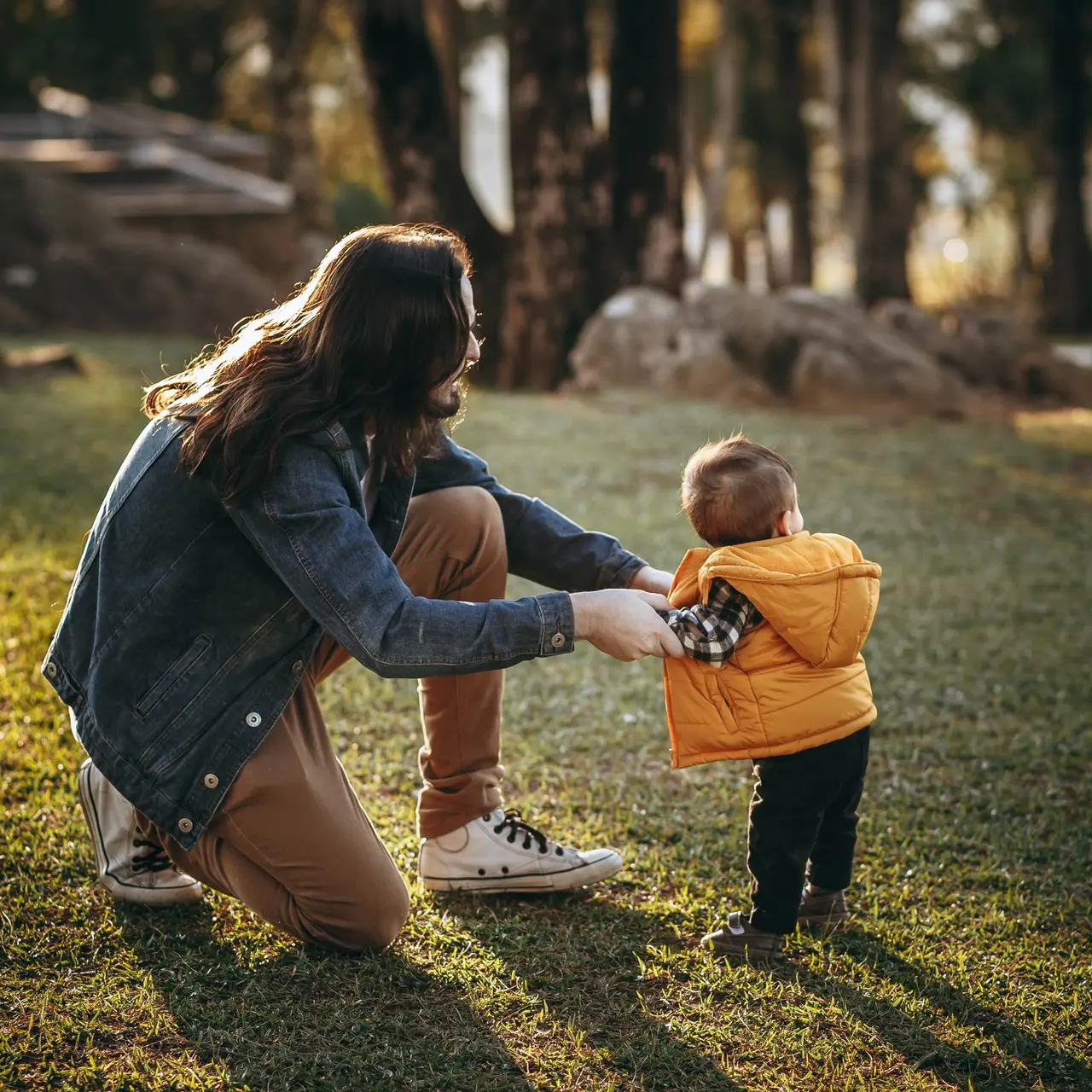 Parent and Child Bonding in Nature A parent crouches down to interact with a toddler in a grassy area, with warm sunlight filtering through trees in the background.