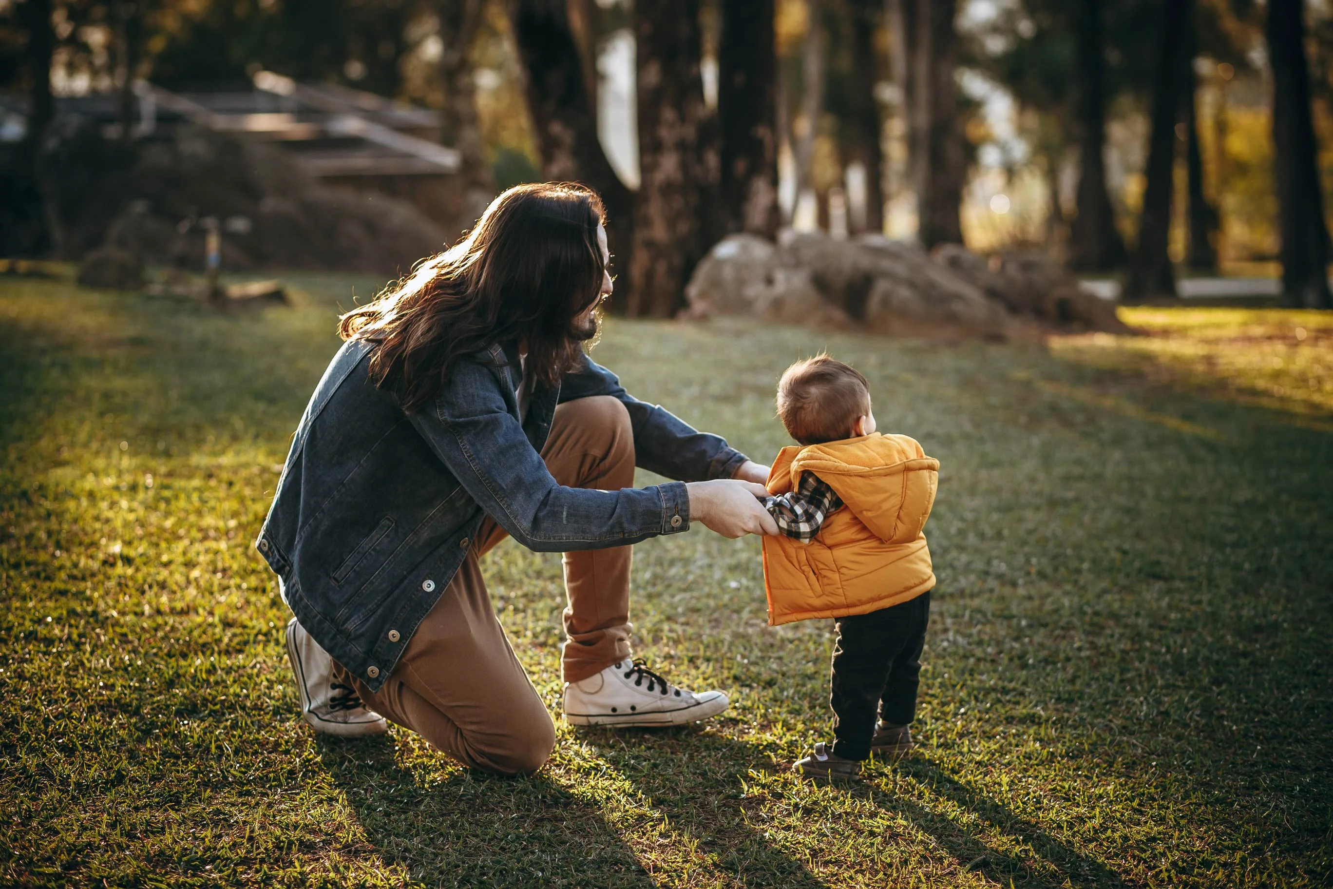 Parent and Child Bonding in Nature A parent crouches down to interact with a toddler in a grassy area, with warm sunlight filtering through trees in the background.