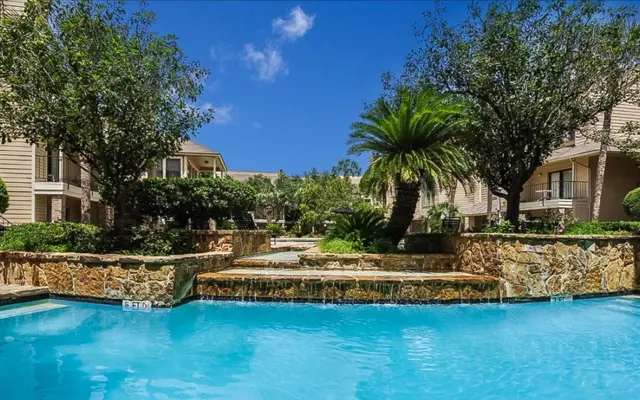 Tranquil Poolside Oasis A scenic view of a swimming pool surrounded by lush greenery and palm trees in a resort-like setting.