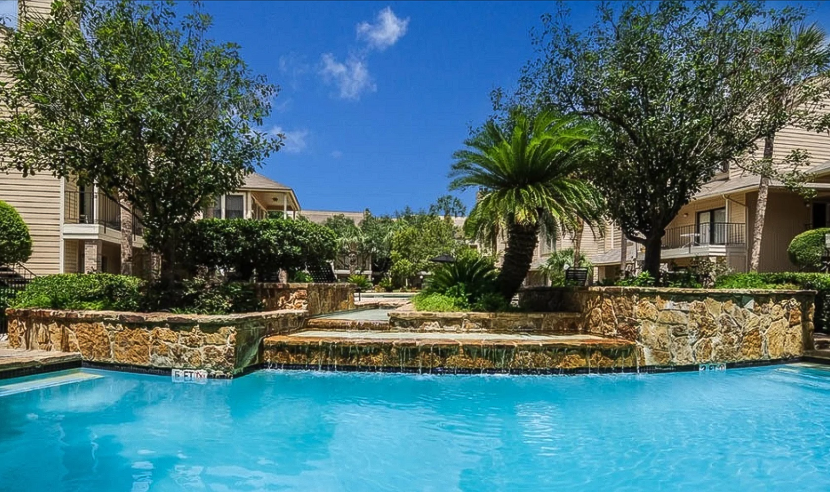 Tranquil Poolside Oasis A scenic view of a swimming pool surrounded by lush greenery and palm trees in a resort-like setting.