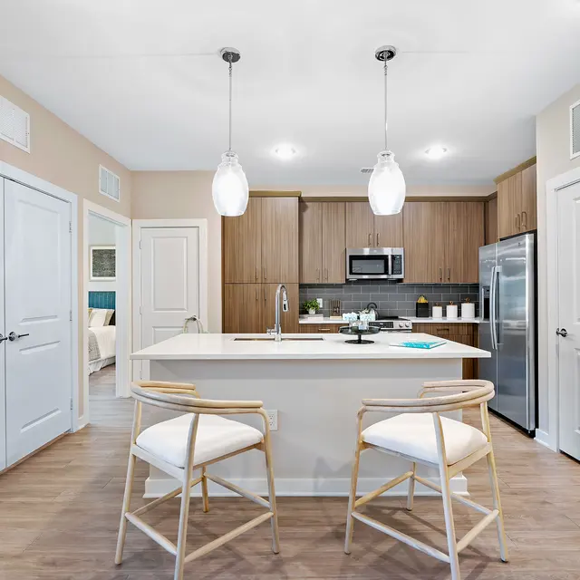 Modern Kitchen Design A modern kitchen featuring an island with two white stools, pendant lighting, wooden cabinets, a stainless steel refrigerator, and an open layout.