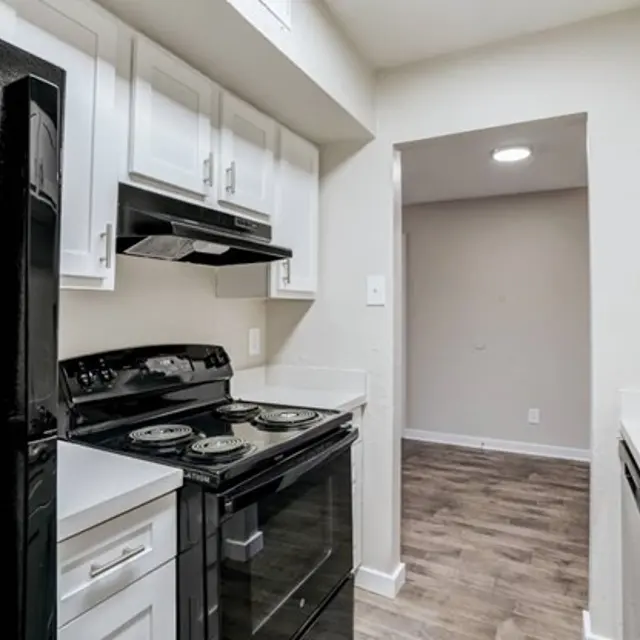 A modern kitchen featuring black appliances, white cabinetry, and light wood flooring. An opening leads to another room.