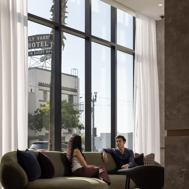 Two people having a conversation in a modern lobby with large windows and natural light.