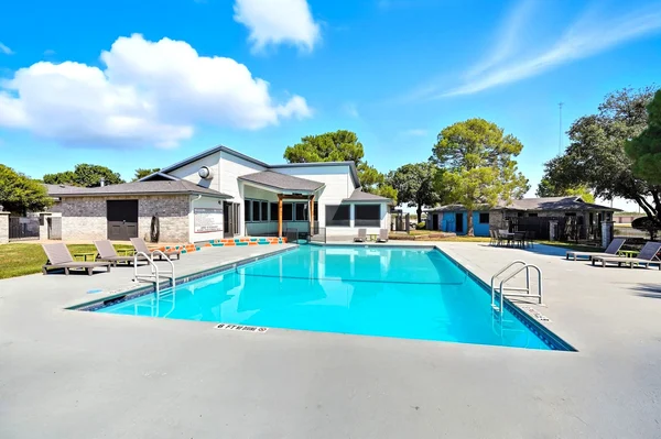 A bright outdoor swimming pool surrounded by lounge chairs and trees on a clear day.