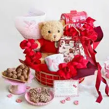 A beautifully arranged Valentine's Day gift basket featuring a teddy bear, chocolate treats, and pink decor.