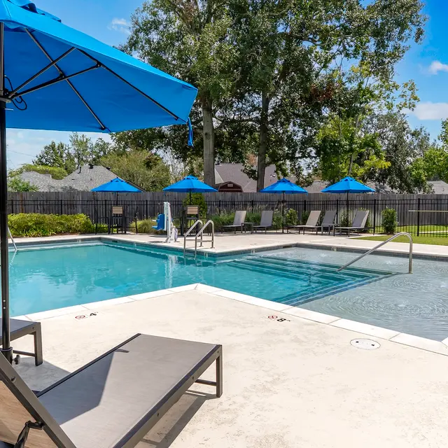 Sunny Poolside Retreat A clear swimming pool surrounded by lounge chairs and blue umbrellas on a sunny day.