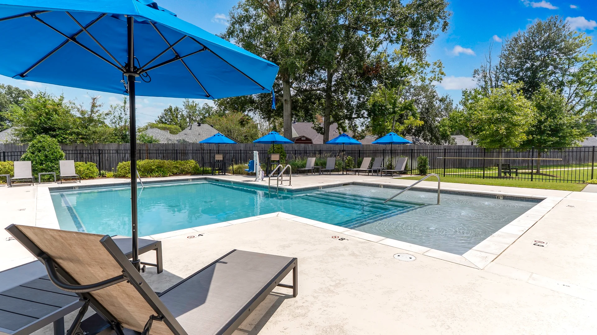 A clear swimming pool surrounded by lounge chairs and blue umbrellas on a sunny day.