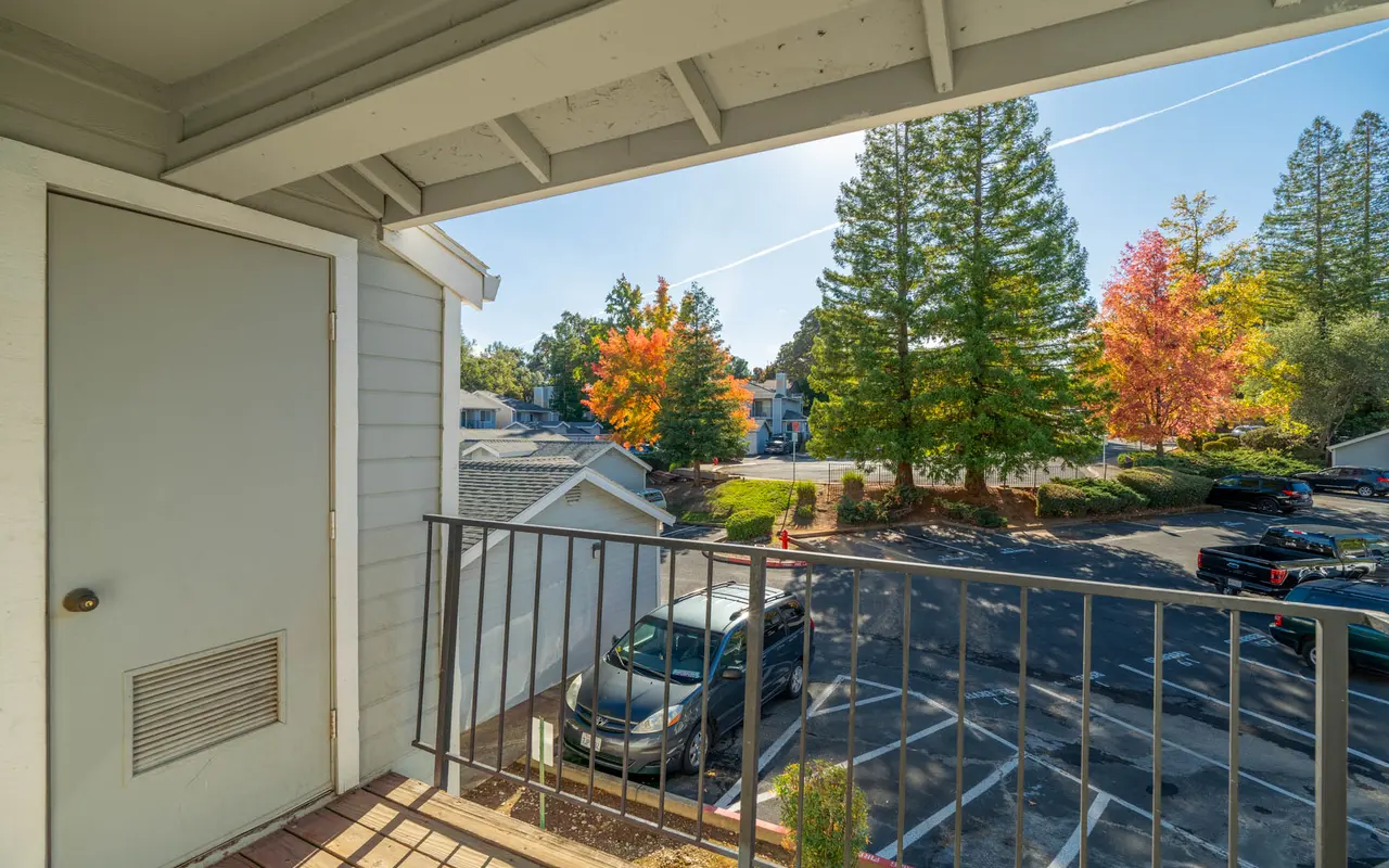 A view from a balcony overlooking a parking area and trees in autumn colors.