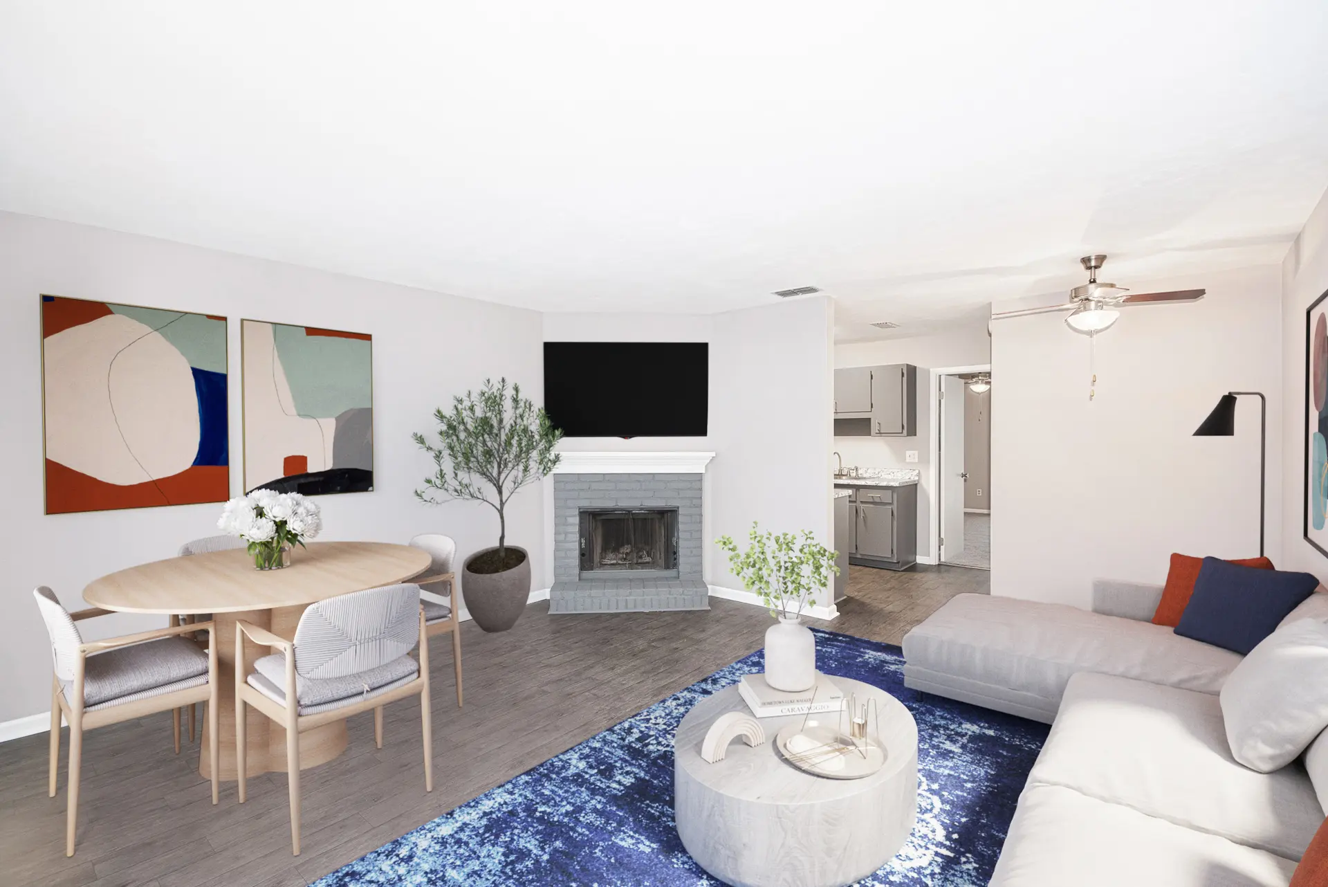 A modern living room featuring a dining area with a round wooden table and chairs, a cozy sectional sofa, and a fireplace. The room is decorated with vibrant artwork and has a blue area rug.