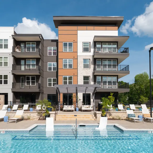 View of a modern apartment complex with a swimming pool and lounge chairs.