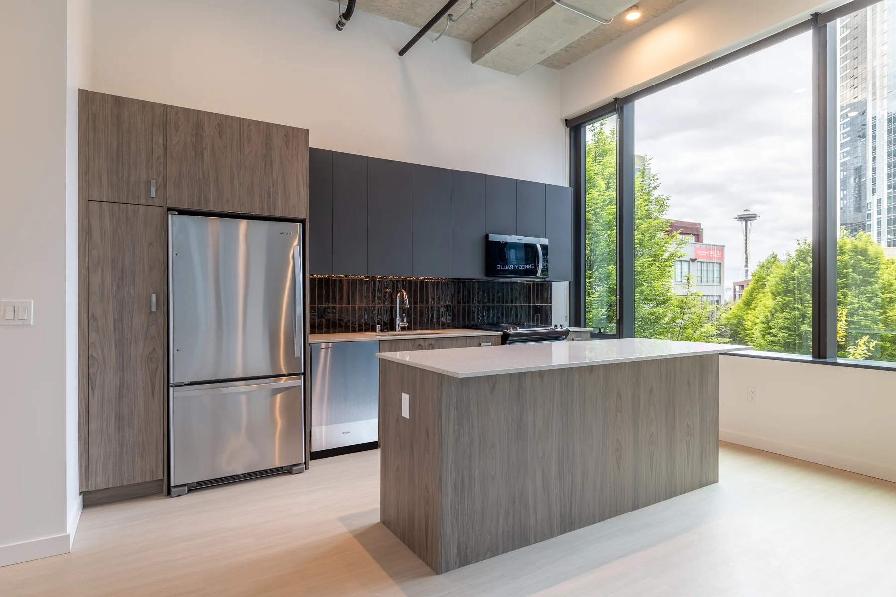 Contemporary Kitchen Design with Natural Light A modern kitchen with a grey and black color scheme, featuring stainless steel appliances, a large island, and large windows providing natural light and views of greenery outside.