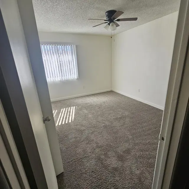 Empty Bedroom Interior A view of an empty bedroom with beige carpet, a ceiling fan, and vertical blinds on a window.