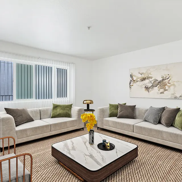 A modern living room with two beige sofas, decorative pillows, a marble coffee table, and a potted plant in the corner.