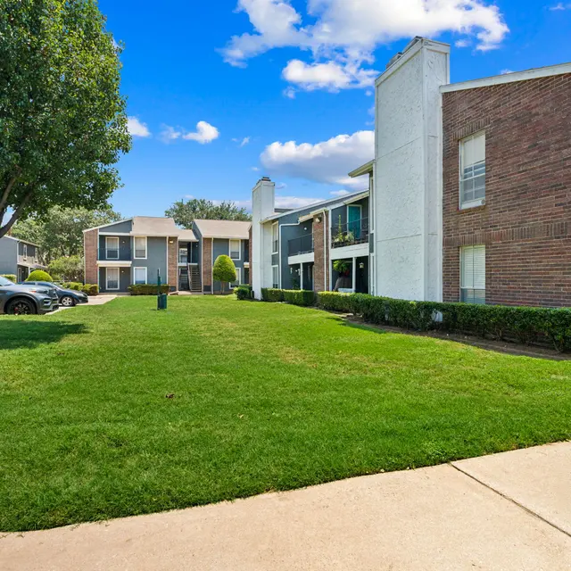 A well-kept apartment complex with two buildings surrounded by grass and trees on a sunny day.