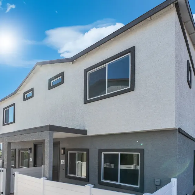 Modern Two-Story House Exterior A modern two-story house with a white exterior, multiple windows, and a covered porch. The house is surrounded by a white fence and features a sunny blue sky with fluffy clouds in the background.