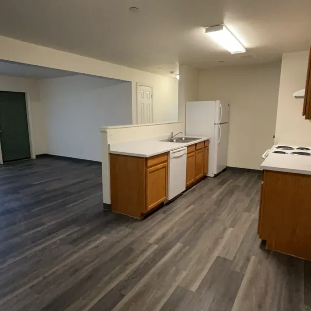 Interior view of a modern open kitchen and living area with a refrigerator, stove, and cabinets.