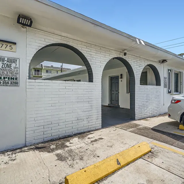 Exterior view of a white brick building with an archway entrance and a parked car in the parking area.